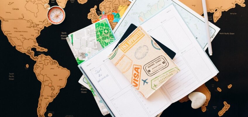 Flat lay of a world map with a compass, travel notes, and a passport displaying visa stamps, symbolizing the journey and preparation for international travel.