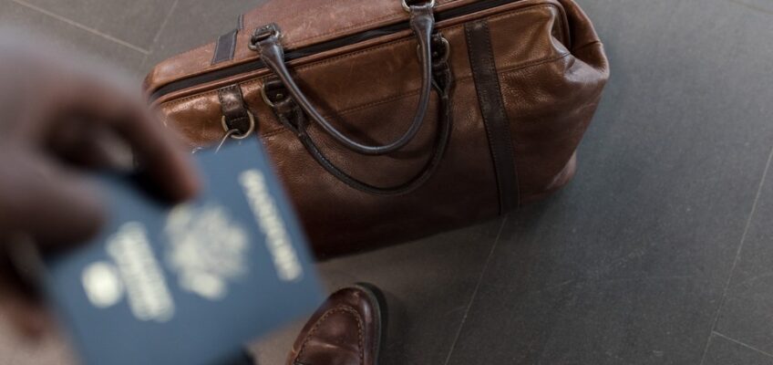 A person holding a passport with a bag on the ground.