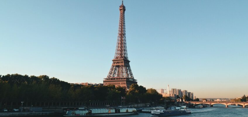 Scenic view of the Eiffel Tower in Paris at sunset with the Seine River and boats in the foreground.