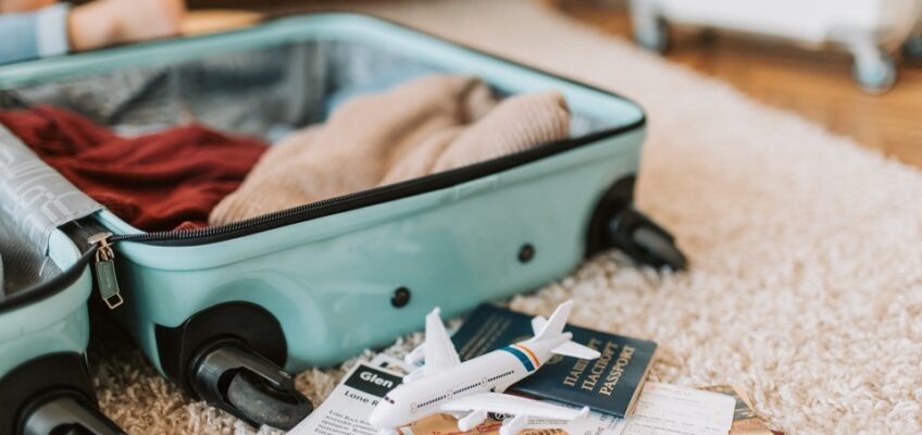 Open suitcase on a carpeted floor with clothing, a toy airplane, and travel documents, symbolizing trip preparation.