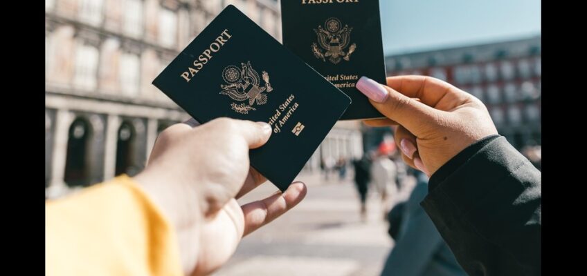 Two hands holding United States passports in front of a historic building, symbolizing international travel.