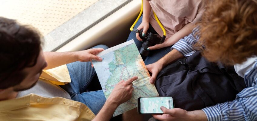 Three travelers engaged in trip planning, with one holding a physical map and another using a mobile phone, indicative of group travel coordination.