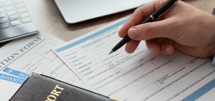 Close-up of a person's hands filling out an ETIAS application form with a pen, with a passport in view, representing the process of applying for ETIAS with a new name.