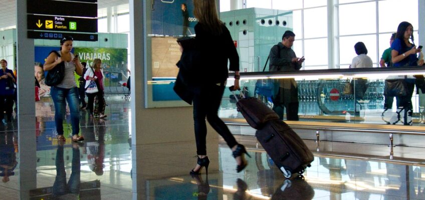 Travelers at a European airport terminal, checking flight details and walking with luggage, reflecting the concept of European travel with ETIAS authorization.