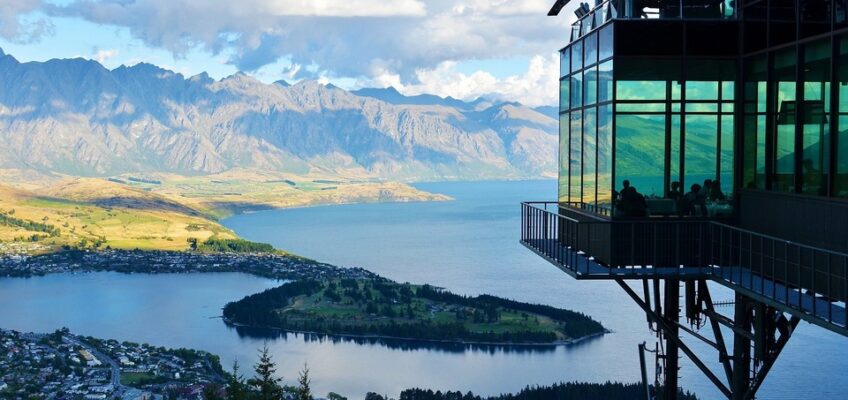 View from a cliff-top observation deck over Queenstown, New Zealand, with the Remarkables mountain range in the background and Lake Wakatipu below.