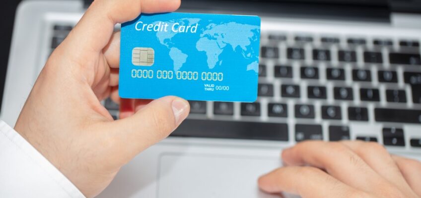 Close-up of a person's hand holding a blue credit card over a laptop keyboard, symbolizing online payment.