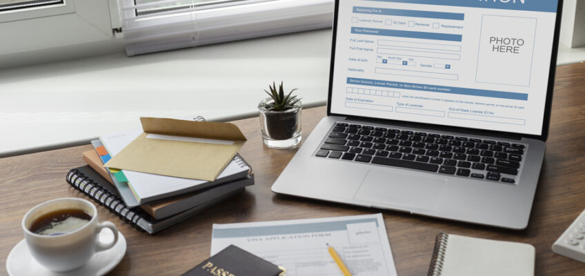 A workspace with a laptop displaying a visa application form, a passport, a coffee cup, notebooks, and writing materials, symbolizing the process of applying for a New Zealand eTA online.