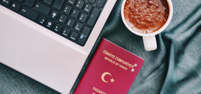 A Turkish passport placed next to a laptop and a cup of coffee, symbolizing the planning and online application process for ETIAS travel authorisation.