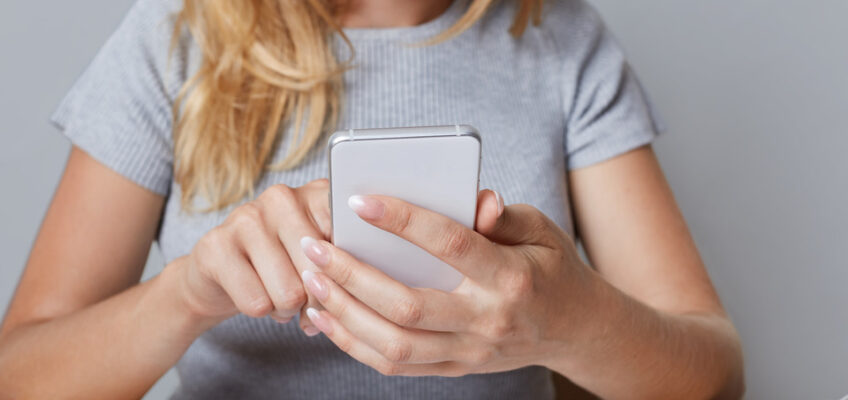 A woman sitting at a desk, reviewing documents and using her smartphone, possibly researching how to apply for a Turkish eVisa after a name change.