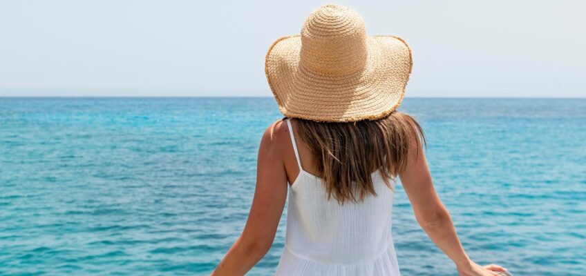 A woman in a white dress and straw hat standing at the ship's railing, gazing out over the blue sea, symbolizing travel and the contemplation of visa requirements for entering Turkey by sea.