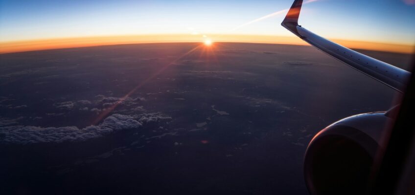 A view from an airplane window during flight capturing a wing over the landscape at sunset