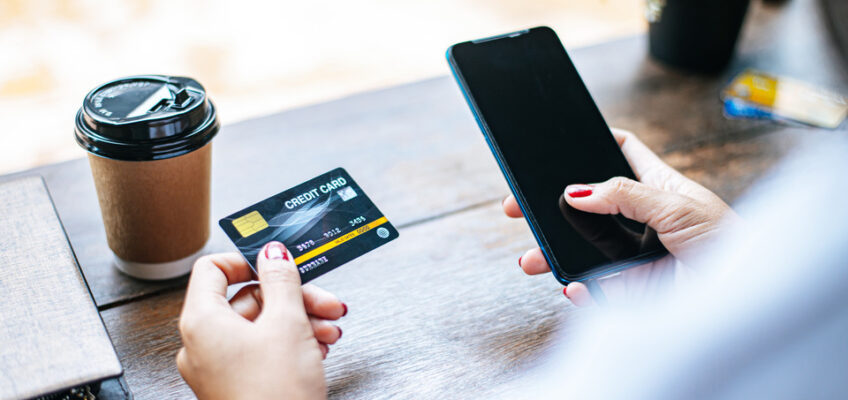 A person holding a credit card in one hand and a smartphone in the other, ready to make an online payment.