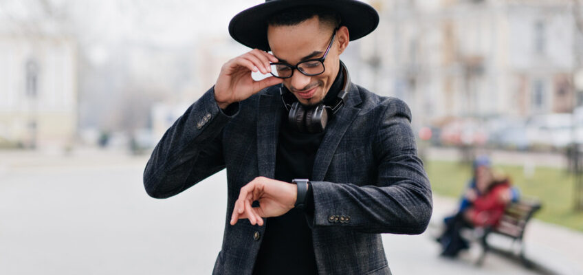 A stylish man in a black hat and coat checks the time on his wristwatch, embodying the concept of timely travel preparations for a New Zealand eTA.