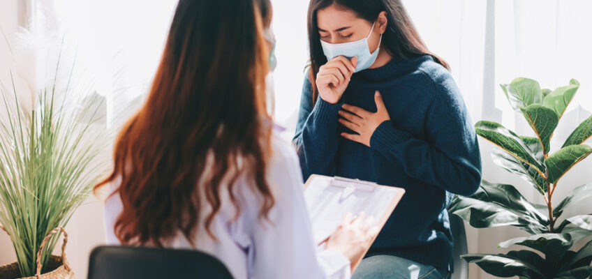 Patient wearing a mask discussing symptoms with a healthcare professional during a medical consultation.