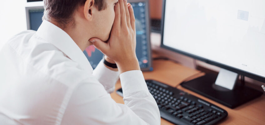 A man in a white shirt appears troubled while looking at a computer screen, with his hands covering his face, possibly reflecting frustration with issues such as those experienced by users of the Turkish eVisa website.