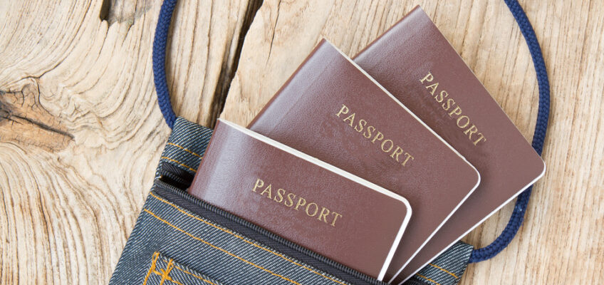 Three passports placed on a denim travel pouch on a wooden surface, suggesting preparation for international travel.