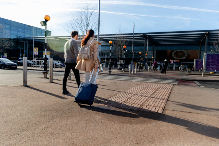 A couple with a suitcase walking hand in hand towards an airport terminal on a sunny day, symbolizing the ease of travel with a New Zealand eTA.