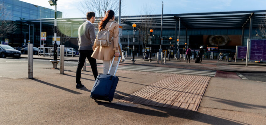 A couple with a suitcase walking hand in hand towards an airport terminal on a sunny day, symbolizing the ease of travel with a New Zealand eTA.