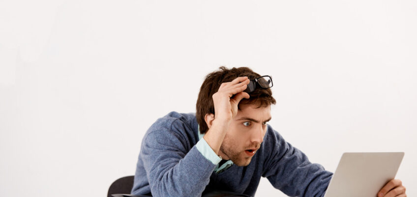 A surprised man in a blue sweater and eyeglasses staring at a tablet with an expression of disbelief, symbolizing confusion over an eVisa rejection.