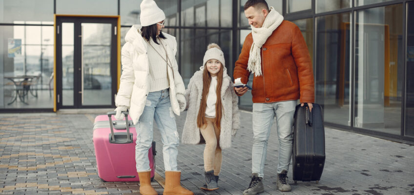 A family of three, with a child holding hands with her parents, smiles while walking outside an airport, ready for their trip, symbolizing the journey minors take when traveling to Turkey with an eVisa.