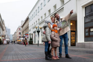 A cheerful family of four, bundled up in warm winter clothes, is exploring a city street together with a map, as the father points out a direction, exemplifying group travel.