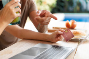 A person pointing at a laptop screen while holding a credit card, indicating the process of making an online payment.