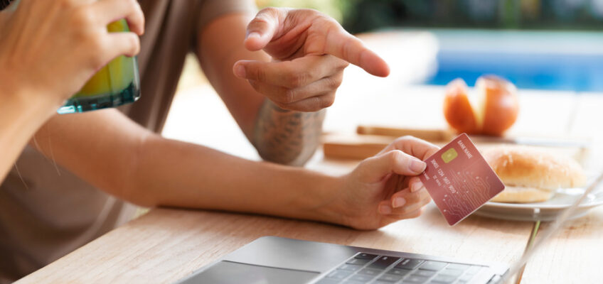 A person pointing at a laptop screen while holding a credit card, indicating the process of making an online payment.