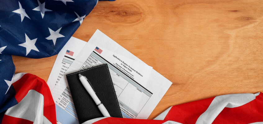 American flag draped over a wooden table with a passport, pen, and ESTA application forms on top, symbolizing the process of applying for a U.S. travel authorization.