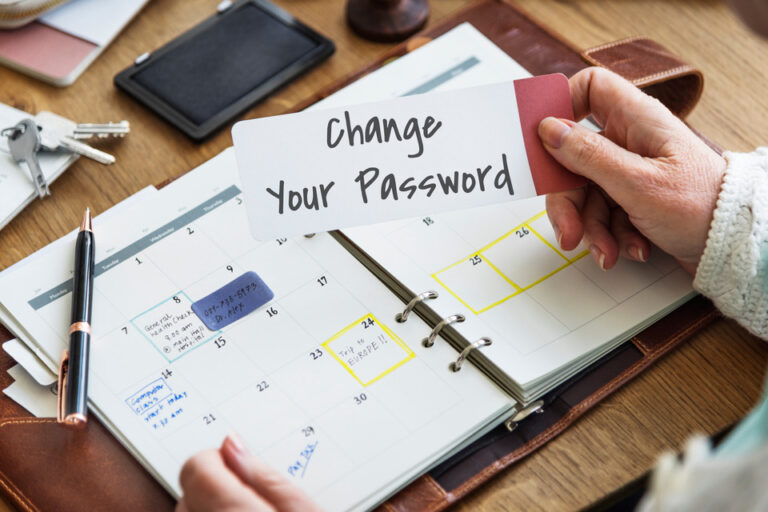 A hand holding a card with the words "Change Your Password" over an open planner, symbolizing proactive personal security measures in the context of online travel authorizations.