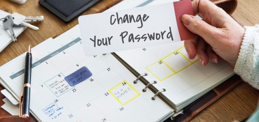 A hand holding a card with the words "Change Your Password" over an open planner, symbolizing proactive personal security measures in the context of online travel authorizations.