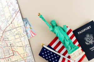 Travel-themed items including a U.S. passport, a miniature Statue of Liberty, and an American flag on top of a map, depicting travel preparations for the United States.