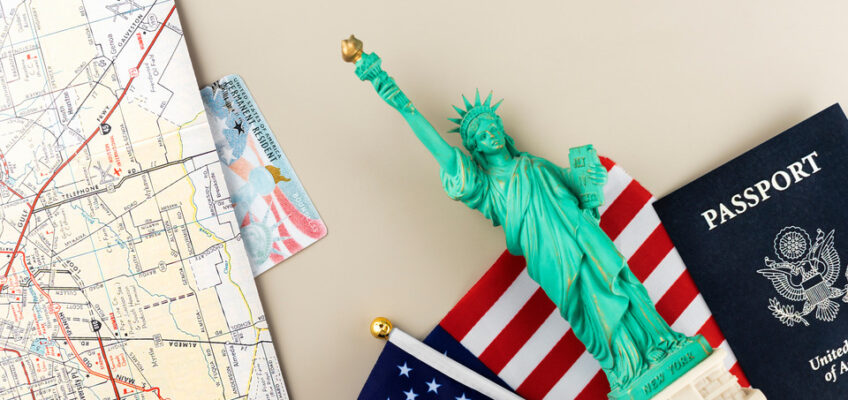 Travel-themed items including a U.S. passport, a miniature Statue of Liberty, and an American flag on top of a map, depicting travel preparations for the United States.