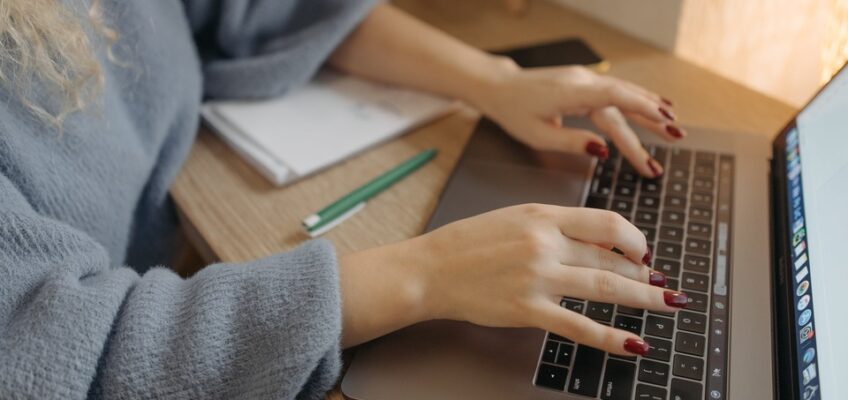 A close-up view of a person's hands typing on a laptop keyboard, suggesting the action of filling out an online form or application.