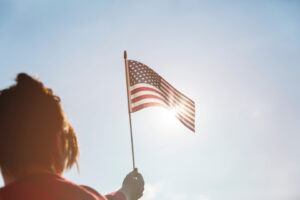 An individual holding up an American flag against a bright sky, symbolizing the patriotic spirit and U.S. travel policies discussed in the history of the U.S. ESTA.