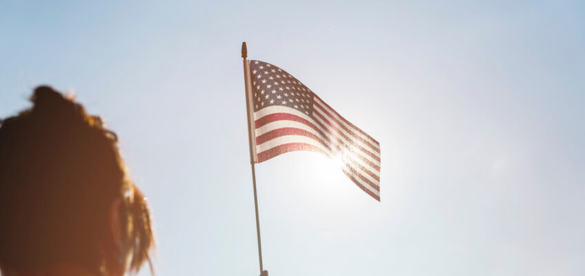 An individual holding up an American flag against a bright sky, symbolizing the patriotic spirit and U.S. travel policies discussed in the history of the U.S. ESTA.