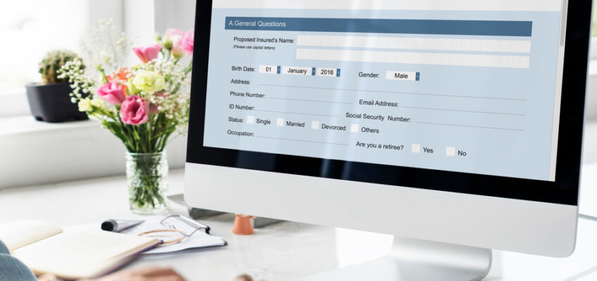 An individual applying online using a desktop computer, with a visible application form on the screen that includes fields for personal details such as name, birth date, gender, marital status, and contact information.