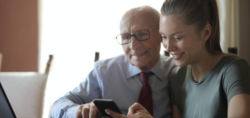 A young woman and an elderly man smiling while looking at a smartphone, possibly researching or discussing travel plans and electronic travel authorizations.