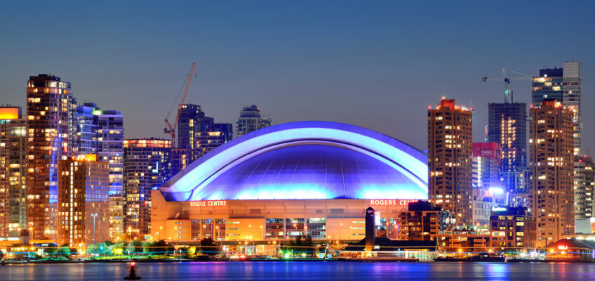 Nighttime view of the Toronto skyline featuring the Rogers Centre, reflecting off the water, symbolizing travel to Canada.