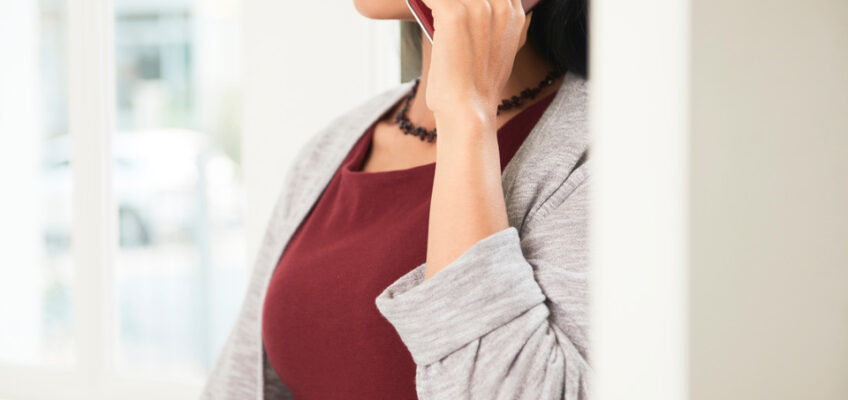 A woman in a burgundy top and gray cardigan speaking on a red phone, representing someone contacting authorities or customer service.