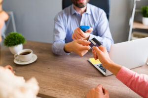 A person handing over a credit card to another individual at a desk, possibly to make a travel booking or payment.