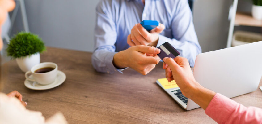 A person handing over a credit card to another individual at a desk, possibly to make a travel booking or payment.