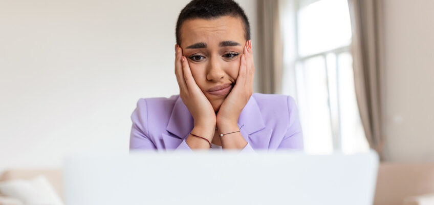 A woman looking distressed while sitting in front of her laptop, possibly after receiving unfavorable news.