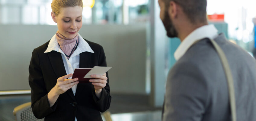 A professional female airport staff member attentively checks a passenger's travel documents at the check-in desk, while a male traveler waits for the verification process to be completed.