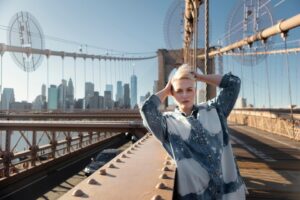 A woman stands on the Brooklyn Bridge with the New York City skyline in the background, symbolizing travel and exploration in the U.S. under an ESTA.