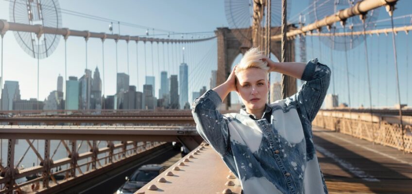 A woman stands on the Brooklyn Bridge with the New York City skyline in the background, symbolizing travel and exploration in the U.S. under an ESTA.