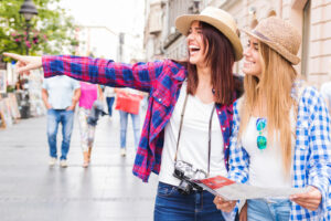 Two joyful female tourists exploring the city streets with one pointing in the distance and the other holding a map, embodying the ease and excitement of traveling on a U.S. ESTA.