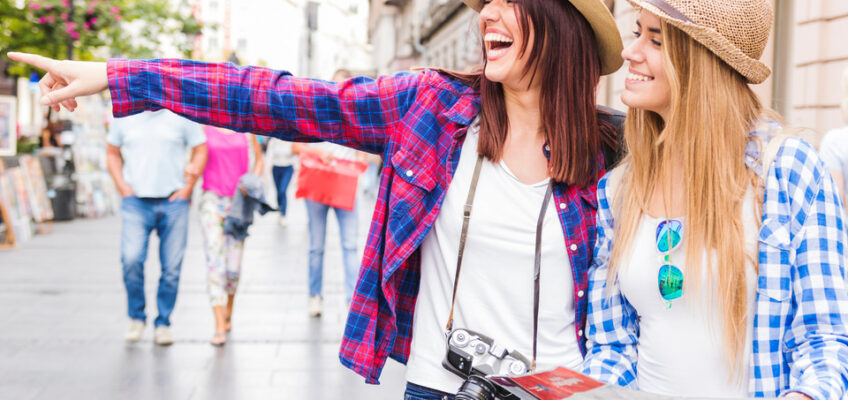 Two joyful female tourists exploring the city streets with one pointing in the distance and the other holding a map, embodying the ease and excitement of traveling on a U.S. ESTA.