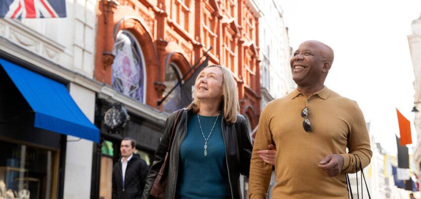 A cheerful mature couple is walking on a UK street adorned with the UK flag, possibly discussing travel plans that could involve renewing their UK Electronic Travel Authorization (ETA).