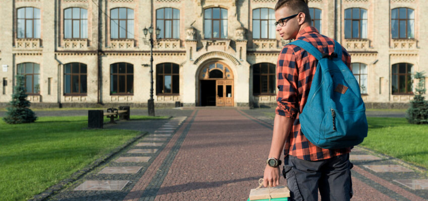 A student with a backpack and a stack of books is walking toward a grand, historic university building, representing the journey of international education and the potential need for travel documentation like student visa.