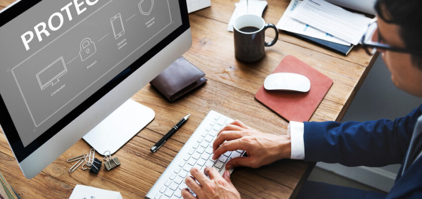 A man, and a computer screen displaying "protection", a cup of coffee, a wallet and other office stuffs.